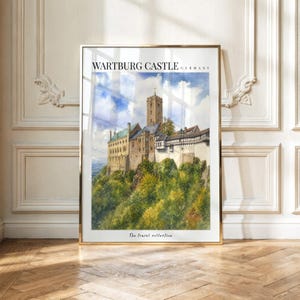 May include: A vertical wall art print featuring a watercolor painting of Wartburg Castle in Germany. The image displays a stone castle with a tall tower atop a lush green hill under a blue sky. The text reads WARTBURG CASTLE GERMANY and The Travel collection.
