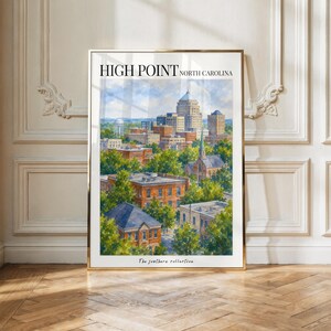 Pode incluir: Uma impressão artística emoldurada com uma aguarela da paisagem urbana de High Point, Carolina do Norte. A pintura mostra vários edifícios, estruturas de tijolo e árvores verdes sob um céu azul. O texto no topo diz High Point North Carolina.