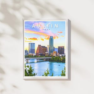 May include: A framed print featuring the Austin, Texas skyline at sunset. The image showcases the city's buildings, a bridge over a river, and the text "AUSTIN TEXAS" at the top. The sky is a mix of pink, orange, and blue.