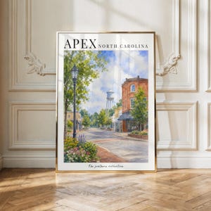 Puede incluir: Una impresión artística vertical con una acuarela de una escena callejera en Apex, Carolina del Norte. La imagen muestra un edificio de ladrillo, una torre de agua, una farola y flores coloridas. El texto dice APEX NORTH CAROLINA y The southore collection.