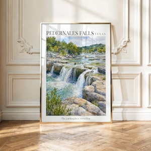 May include: A vertical rectangular art print in a gold frame featuring a watercolor painting of Pedernales Falls in Texas. The image depicts a cascading waterfall over layered rock formations with green trees and blue water. Text reads Pedernales Falls Texas.