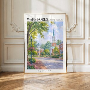 May include: A framed art print featuring a watercolor painting of the Wake Forest, North Carolina campus. The scene depicts a brick building with a tall steeple, a paved path, green trees, and a black lamppost. Text reads Wake Forest North Carolina.