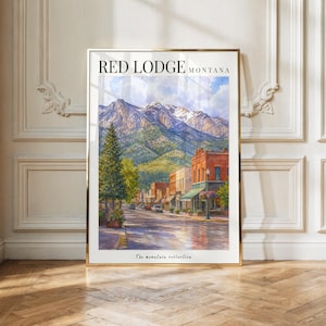 May include: A framed vertical art print titled RED LODGE MONTANA featuring a watercolor painting of a town street with brick buildings, a tall evergreen tree, and snow-capped mountains in the background under a cloudy sky, with The mountain collection text.