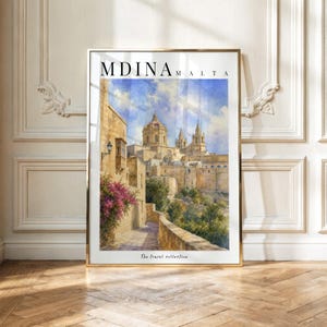 Könnte beinhalten: Ein gerahmter vertikaler Kunstdruck mit einem Aquarell von Mdina, Malta. Das Bild zeigt Steingebäude, eine Kathedrale mit Kuppel und rosa Bougainvillea-Blüten entlang eines Weges. Der Text MDINA MALTA und The travel collection sind zu sehen.