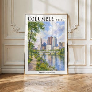 May include: A vertical art print featuring a watercolor painting of the Columbus, Ohio skyline across a river. The scene includes a tree-lined path, a bridge, and city buildings under a blue sky. The text reads COLUMBUS OHIO and The midwestern collection.