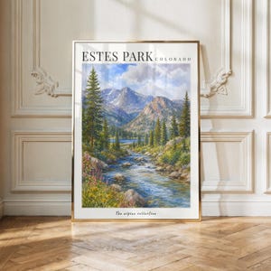 May include: A vertical rectangular art print in a gold frame featuring a landscape painting of Estes Park, Colorado. The scene depicts a flowing river, evergreen trees, and mountains under a blue sky. Text reads ESTES PARK COLORADO and The alpine collection.
