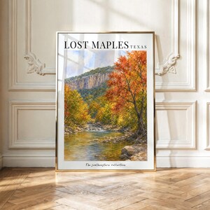 Peut inclure: Une impression d'art mural rectangulaire verticale représentant un paysage de Lost Maples au Texas. L'image montre une rivière coulant devant des arbres aux feuillages d'automne dans des tons orange, jaune et vert, avec une falaise rocheuse.