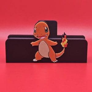 Op de afbeelding: Een zwarte houten bureau-organizer met een kleurrijk Charmander-personage. De Charmander is oranje, bruin en wit met een vlam op zijn staart. De organizer heeft een rechthoekige vorm met een sleuf voor het vasthouden van items. De achtergrond is effen rood.