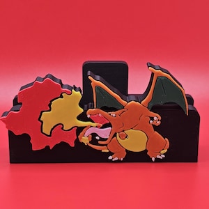 Può includere: Un organizer da scrivania nero con un design colorato di Charizard. Il Charizard arancione, giallo e verde è raffigurato mentre sputa fuoco. L'organizer ha un design a fiamma rossa, gialla e nera sul lato sinistro.