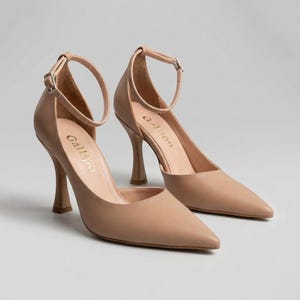Peut inclure: Une paire d'escarpins beiges &agrave; talons hauts, avec des bouts pointus et des brides de cheville. Les talons mesurent environ 9 cm de haut. La marque "Gallipo" est imprim&eacute;e sur la semelle int&eacute;rieure. Les chaussures sont en mati&egrave;re lisse, semblable au cuir.