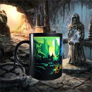 May include: Black ceramic mug featuring a vibrant illustration from "The Lord of the Rings." The design showcases a green landscape with figures and the text "THE LORD" in gold. A black handle completes the mug.