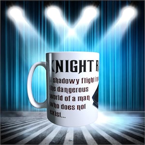 以下が含まれることがあります： 黒色の「KNIGHT R」という文字と、マルーン色のテキストが書かれた白いセラミックマグカップ。テキストは「shadowy flight in the dangerous world of a man who does not exist...」と書かれています。マグカップは、青と白の照明のあるステージに置かれています。