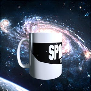 May include: A white ceramic mug featuring a black horizontal band with the white text SPACE THE FINAL FRONTIER printed in a bold sans-serif font. The mug has a curved handle on the left side and a smooth, glossy finish on its exterior surface.