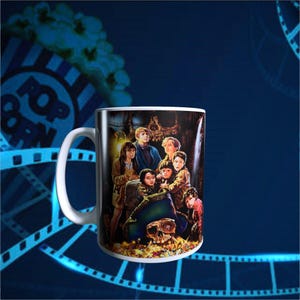 May include: White ceramic mug featuring a movie poster design with a group of children and a treasure chest. The mug has a curved handle and a glossy finish, perfect for coffee or tea.