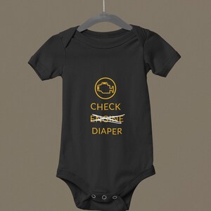 May include: Black baby bodysuit with a yellow engine graphic and the words "CHECK DIAPER", with "ENGINE" crossed out. The bodysuit has short sleeves and three poppers at the bottom.
