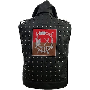 May include: Black leather vest with a hood and silver studs. The back features a patch with a stylized face design in red, brown, and silver. The vest is sleeveless and has a classic biker style.