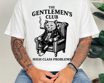 Könnte beinhalten: Weißes T-Shirt mit einer Schwarz-Weiß-Illustration einer Katze im Smoking, die eine Zigarre raucht und eine Tasse hält. Der Text lautet "THE GENTLEMEN'S CLUB" und "HIGH CLASS PROBLEMS".