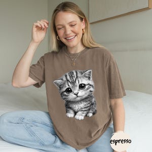 Peut inclure: T-shirt de couleur expresso avec un grand motif d&eacute;taill&eacute; d'un chaton gris et blanc aux grands yeux. Le chaton est centr&eacute; sur le t-shirt. Le t-shirt a des manches courtes et une coupe d&eacute;contract&eacute;e. Le mot "espresso" est imprim&eacute; sur une petite &eacute;tiquette ronde.
