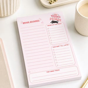 May include: Pink tear-away notepad with the text "Brain Zoomies" and "My Thoughts Have Zoomies." The notepad includes sections for to-do lists and notes, measuring 5" x 7". A black cat graphic is also included.