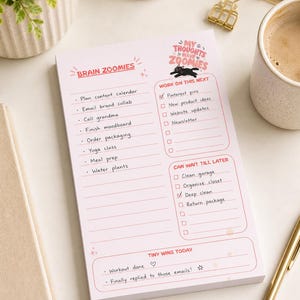 May include: A pink notepad with the words "Brain Zoomies" and "My Thoughts Have Zoomies." The notepad has a to-do list with checkboxes and sections for "Work on this next," "Can wait till later," and "Tiny wins today."