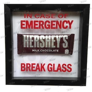 Op de afbeelding: Een ingelijst novelty-bord met een Hershey's Milk Chocolate reep. Het bord leest "IN CASE OF EMERGENCY BREAK GLASS" in rode letters. De lijst is zwart en de achtergrond is wit.