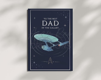 May include: A rectangular greeting card with a dark blue background featuring a light blue starship illustration in the centre. The text reads TO THE BEST DAD IN THE GALAXY above the ship, with a small starfleet-style emblem at the bottom.