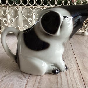 May include: A white ceramic mug with a black handle and the text "But First, Coffee" in a black, bold font. The mug is on a white surface.