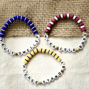 May include: Three handmade beaded bracelets. One is blue with gold accents and the text "VAULT DWELLER". Another is pink, white, and black with the text "NUKA COLA BABE". The third is yellow and blue with the text "PLEASE STAND BY".