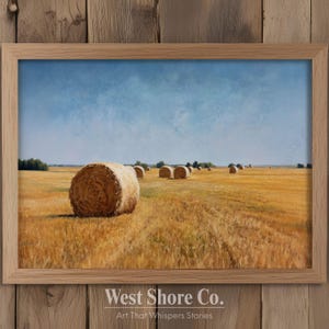 Op de afbeelding: Een ingelijst landschapsschilderij toont een veld met gouden hooibalen onder een blauwe lucht. Het kunstwerk toont verschillende ronde hooibalen verspreid over het veld, met bomen in de verte. Het frame is gemaakt van lichtgekleurd hout.