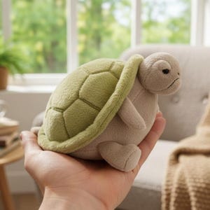 Könnte beinhalten: Ein Kuscheltier in Form einer Schildkröte mit einem hellgrünen Panzer und einem beigefarbenen Körper. Die Schildkröte hat ein detailliertes Panzer-Muster. Das Spielzeug ist als tröstender Begleiter für Kinder konzipiert.