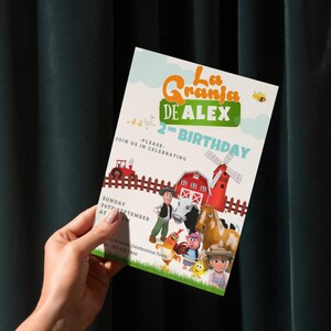May include: A colorful invitation for a 2nd birthday party with a farm theme. The design features cartoon farm animals, a red barn, a windmill, and the text "La Granja DE ALEX 2nd Birthday". The invitation is held by a person.