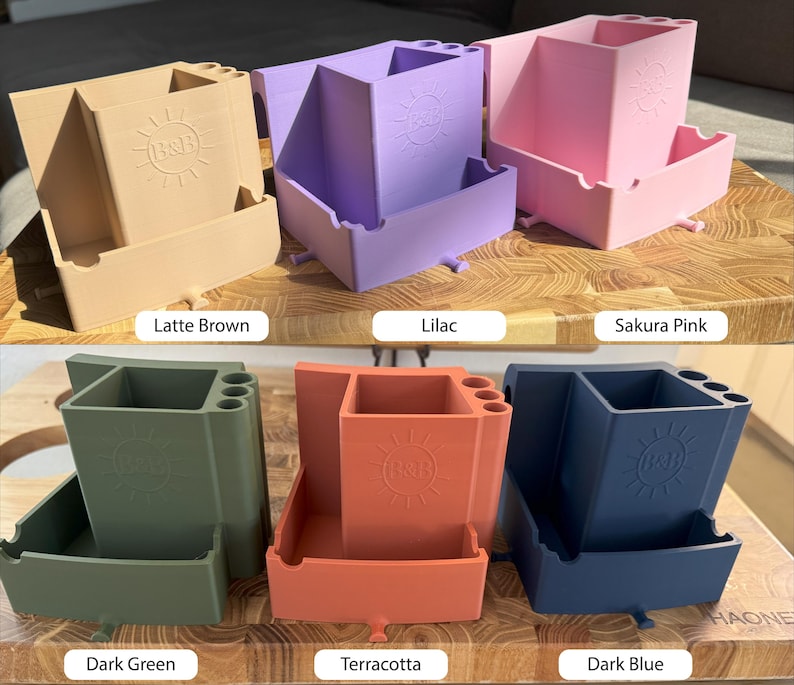 May include: A collection of six multi-compartment desk organizers in various colors: latte brown, lilac, sakura pink, dark green, terracotta, and dark blue. Each organizer features a sun logo and the text "B&B".