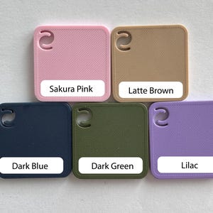 May include: Five square color swatches in Sakura Pink, Latte Brown, Dark Blue, Dark Green, and Lilac. Each swatch has a rounded corner and a curved cutout. Each swatch has a white label with the color name.