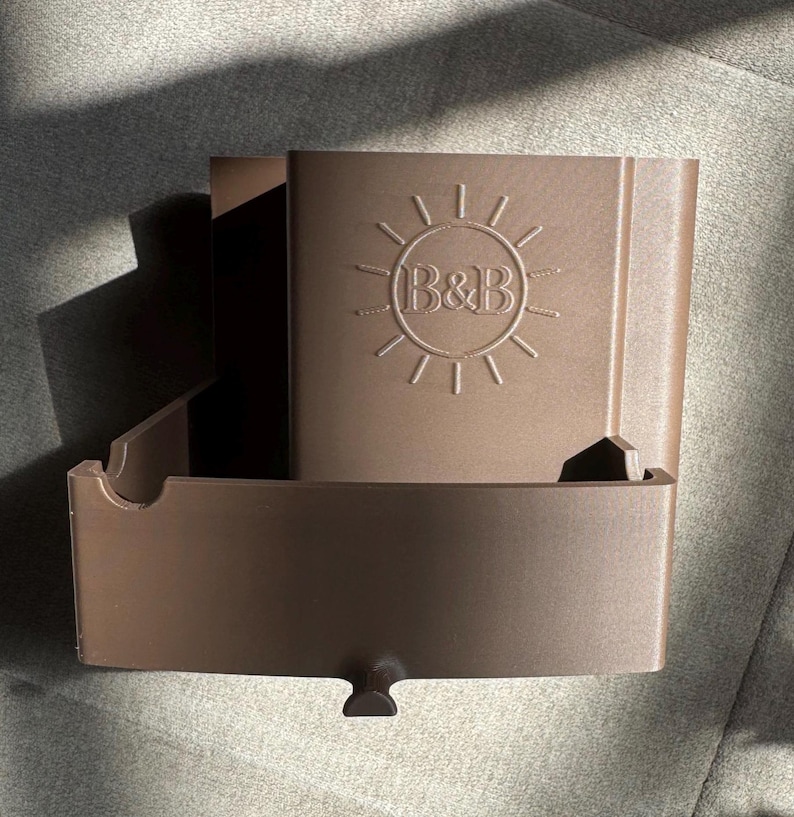 May include: A brown plastic organizer with a sun logo and the letters "B&B" embossed on the front. The organizer has a rectangular shape with an open compartment and a small, curved handle at the bottom.