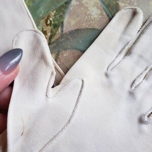 May include: A pair of white cotton gloves with a delicate stitch detail around the edges. The gloves are made of a soft, lightweight fabric and have a classic, elegant design.