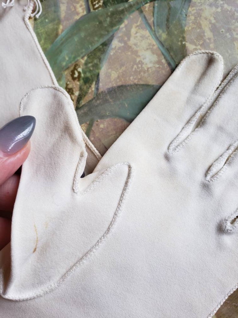 May include: A pair of white cotton gloves with a delicate stitch detail around the edges. The gloves are made of a soft, lightweight fabric and have a classic, elegant design.