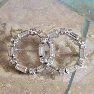 Broche vintage de círculos interconectados con diamantes de imitación transparentes en tono plateado y puntas facetadas.