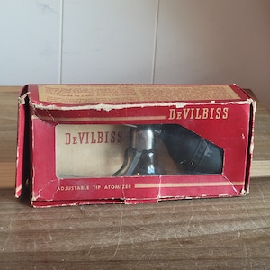 May include: A red box with the words "DEVILBISS ADJUSTABLE TIP ATOMIZER" printed on the front. The box contains a silver atomizer with a black nozzle.