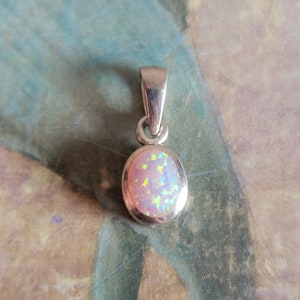 May include: A silver pendant with a light pink oval opal gemstone. The opal has a rainbow iridescent sheen.