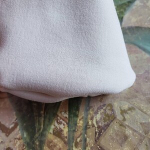 May include: A close-up of a white fabric with a soft, textured surface. The fabric is folded and appears to be a piece of clothing or a home decor item.