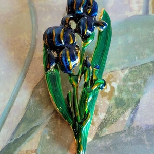 May include: A gold-toned brooch featuring two blue and gold irises with green leaves.