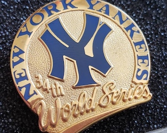 May include: A gold-colored pin with a blue New York Yankees logo and the text "34th World Series".