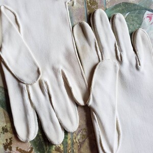 May include: A pair of white cotton gloves with a fringed trim. The gloves are long and have a delicate, feminine look.