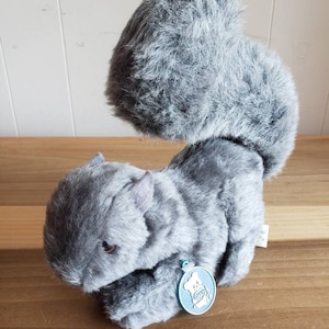 May include: Gray plush squirrel toy with a fluffy tail. The toy has a small tag attached to its paw with a cartoon squirrel on it.