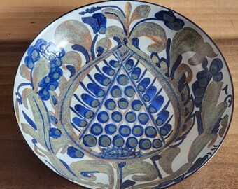 May include: A white ceramic bowl with a blue and brown floral design. The bowl features a central motif of a stylized flower with a geometric pattern.