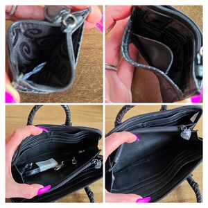 May include: A black leather wallet featuring a zippered main compartment, multiple interior card slots, and a central zippered pocket with a heart-shaped pull. The interior lining is black with a repeating swirl pattern, and the exterior has braided handles.