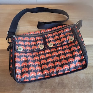 May include: A black canvas shoulder bag with a red floral pattern. The bag has a zipper closure and two front pockets with metal snaps.