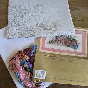 May include: A cross-stitch kit with a floral design, featuring a chart, embroidery floss, and aida cloth. The kit includes a finished size of 20 x 10 inches and a matted size of 24 x 14 inches. The kit is titled "French Floral Basket".