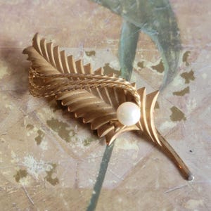 May include: A gold-toned brooch in the shape of a stylized leaf with a single pearl accent.