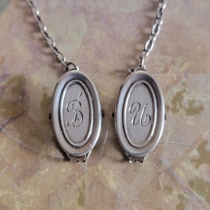 May include: Two silver oval-shaped charms with chains attached. The charms are engraved with the letters "B" and "Ub".
